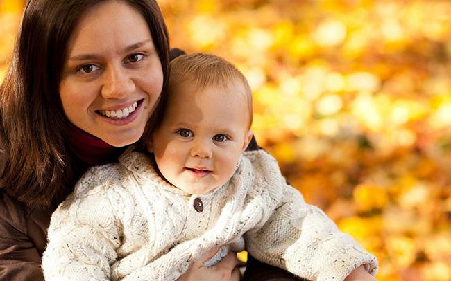 Smiling mother holds baby in outdoor setting